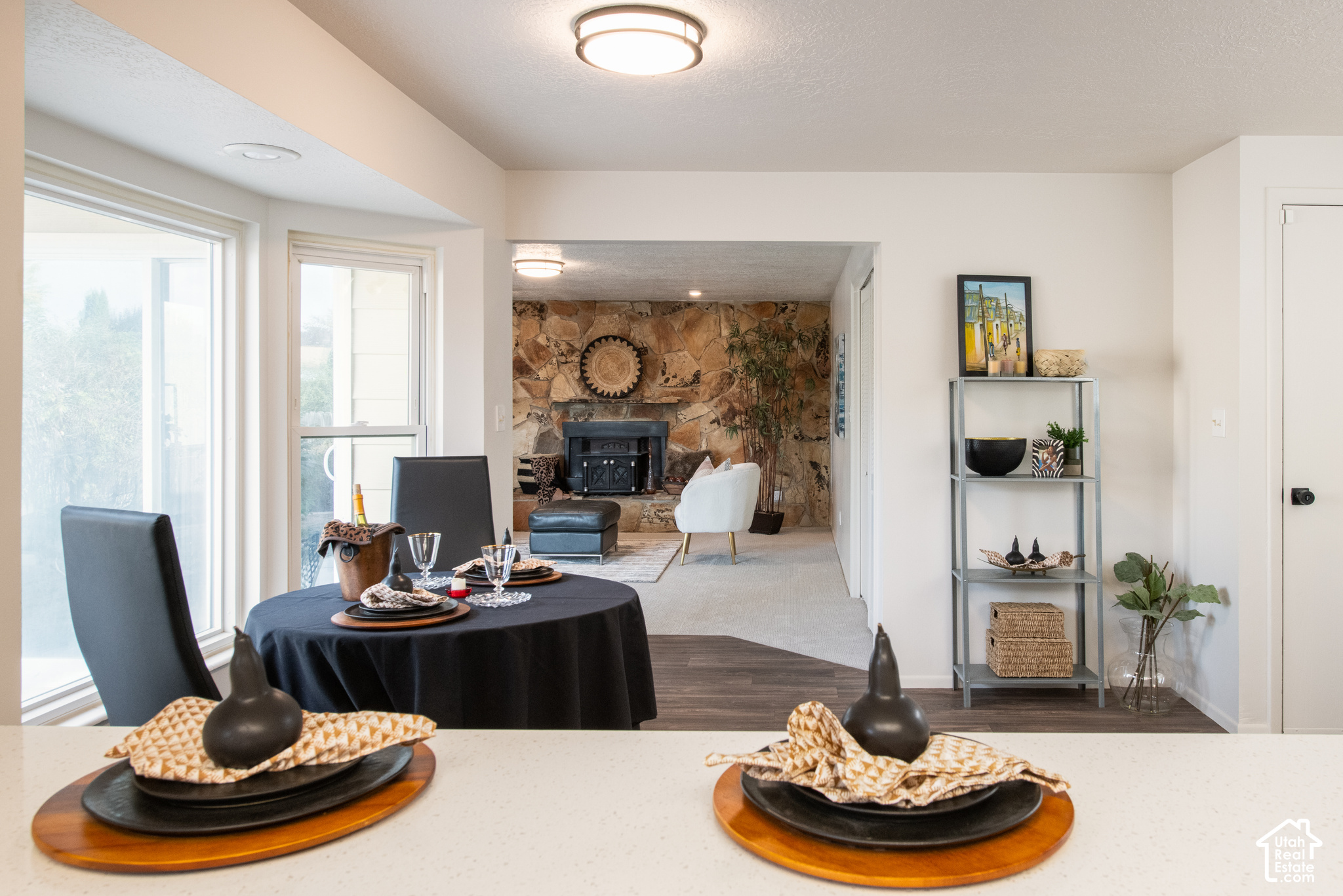 Staged living and dining area with a stone fireplace wall and dining table beside large windows.