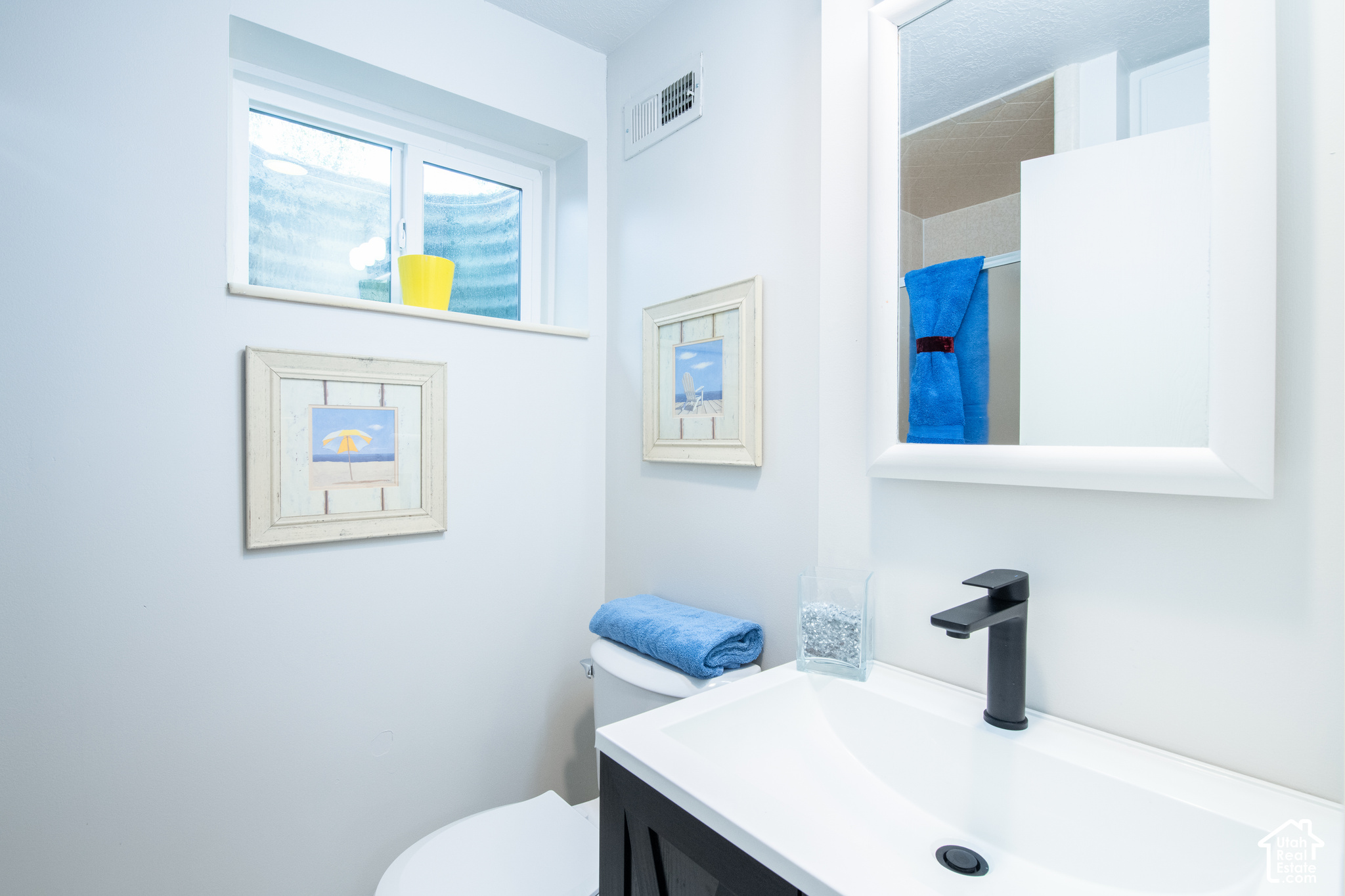 Bathroom with a white sink, black faucet, large mirror, and blue towels.