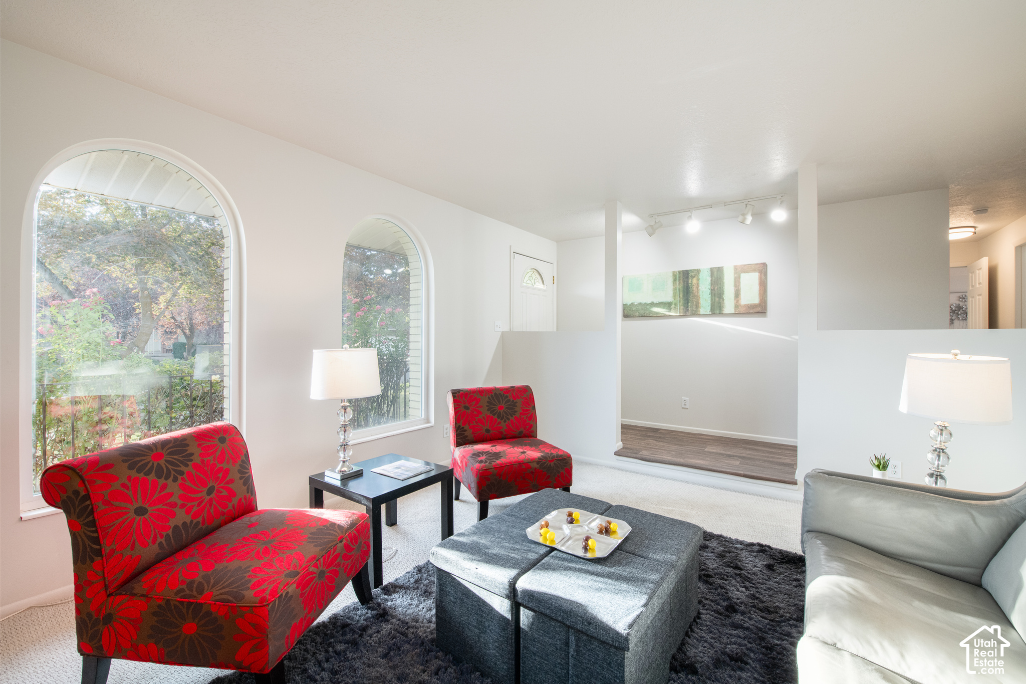 Living room with arched garden-view windows, red floral chairs, and a gray ottoman.