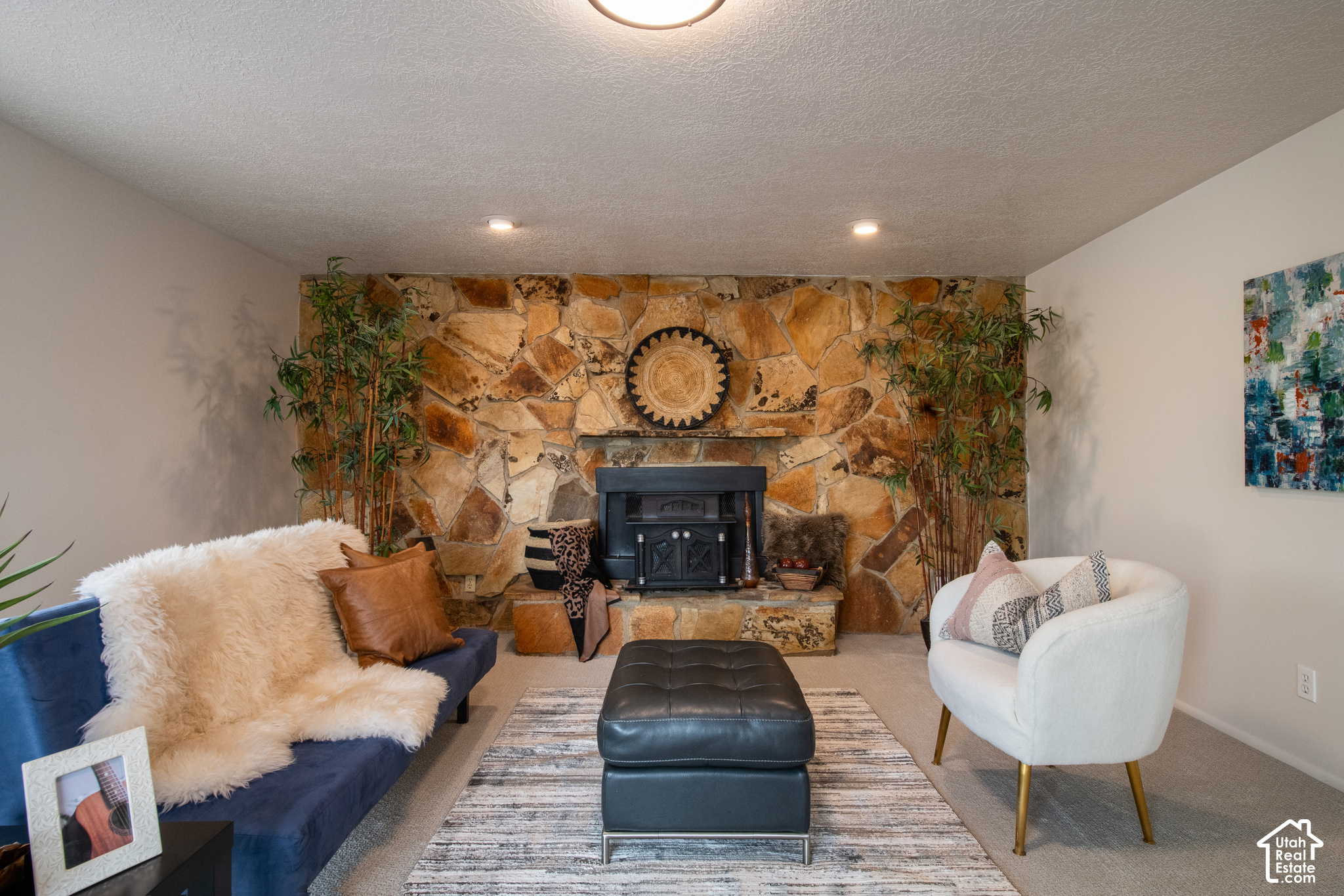 Staged living room with a floor-to-ceiling stone fireplace, navy sofa, white chair, and dark ottoman.