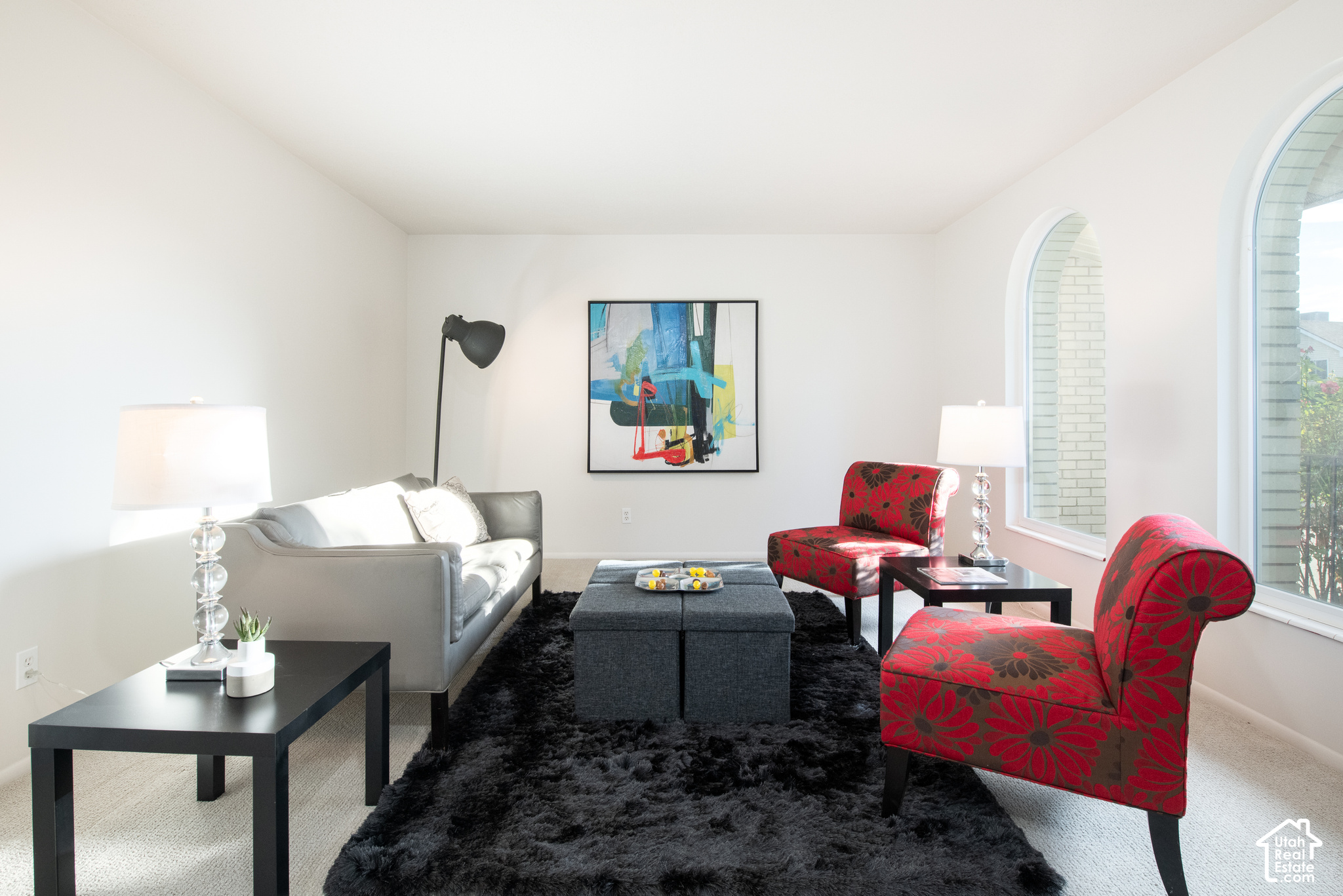 Living room with arched windows, a gray sofa, red floral chairs, and a black shag rug.