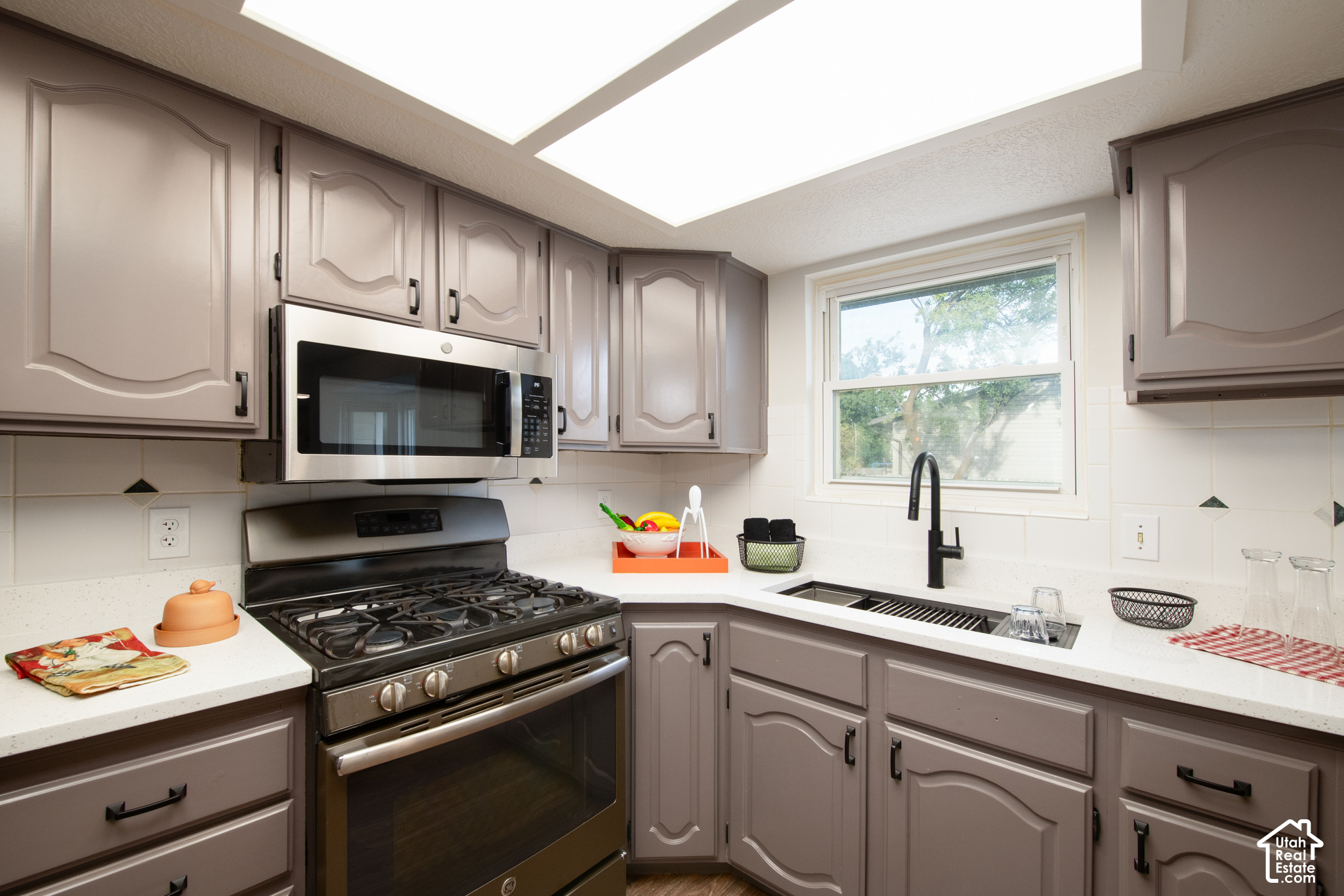 Kitchen with taupe cabinets, stainless appliances, and a sink beneath a large window.