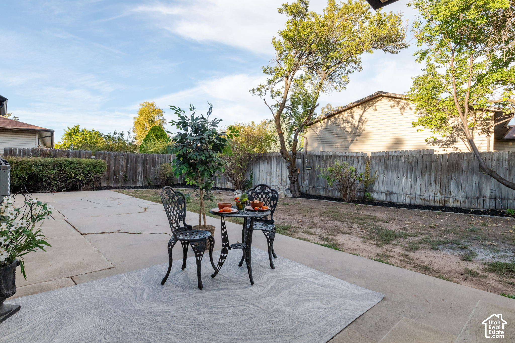 Backyard patio with a black metal dining set, outdoor rug, mature trees, and fenced yard.