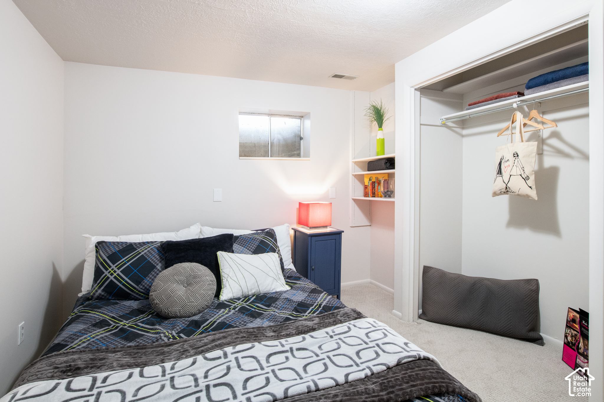 Furnished bedroom with dark plaid bedding, a red bedside lamp, and an open closet.