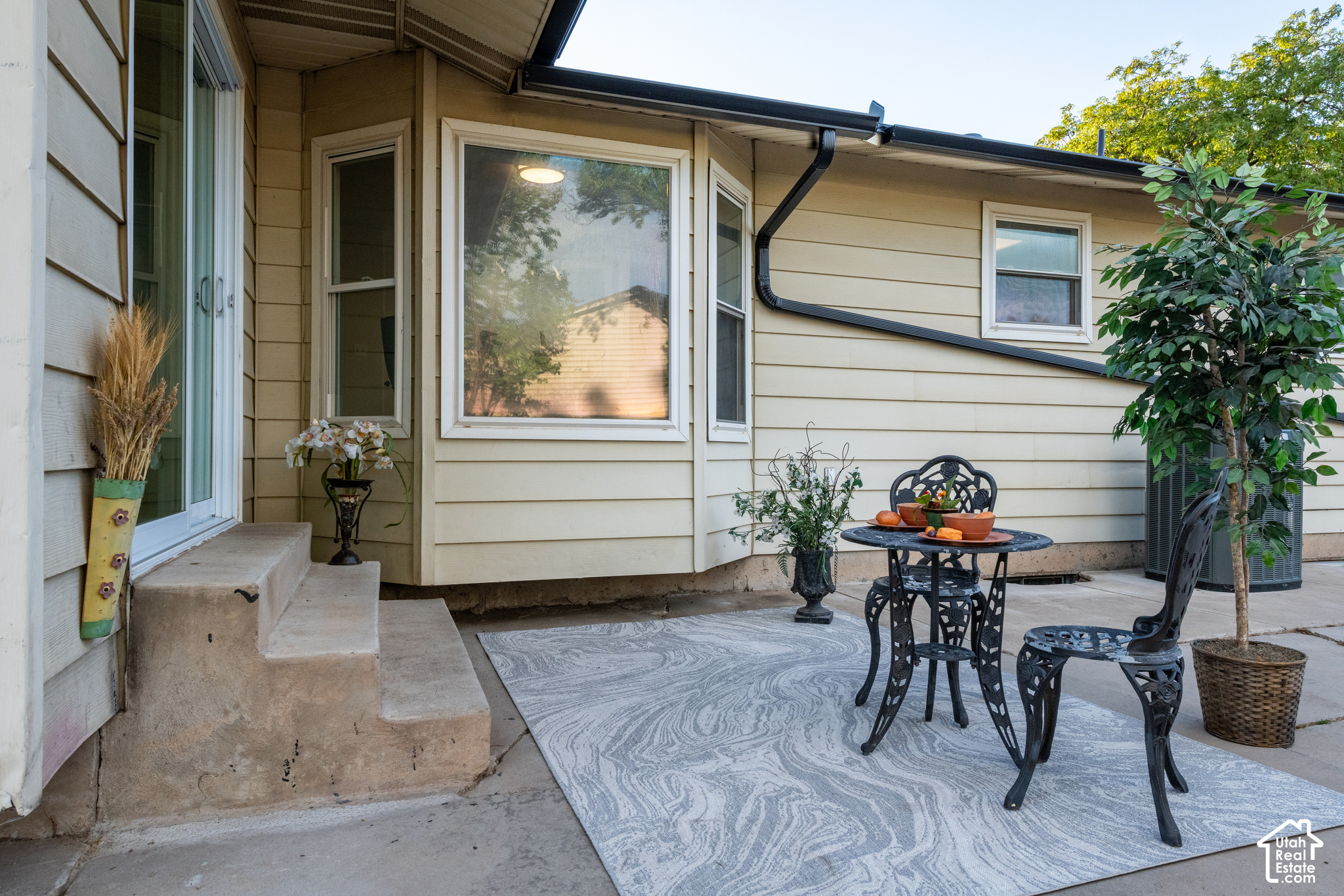 Home patio with black metal seating, patterned rug, potted plants, and sliding glass door.