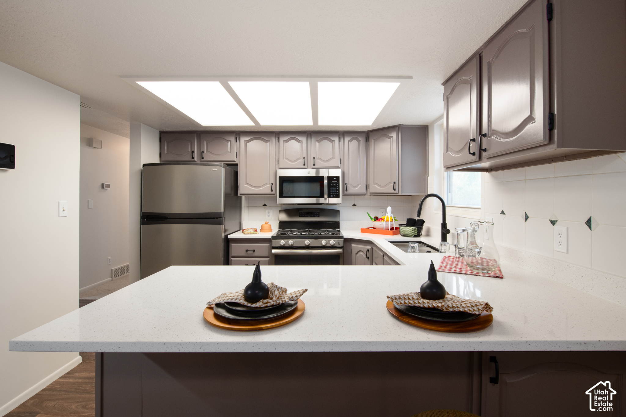 Kitchen with gray cabinets, stainless steel appliances, and a large white island set with place settings.