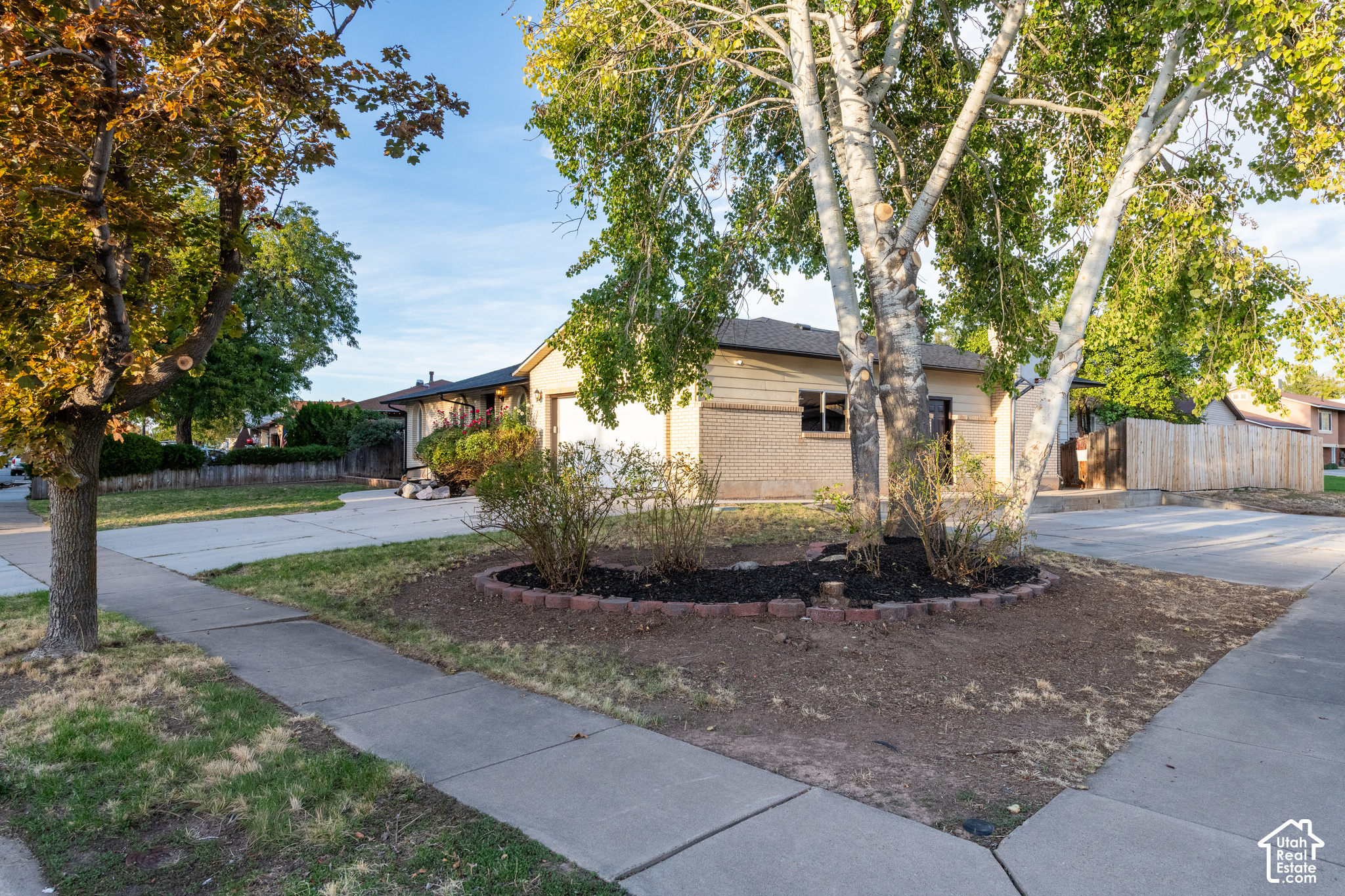 Single-story home framed by mature trees, with a broad driveway and sidewalk.