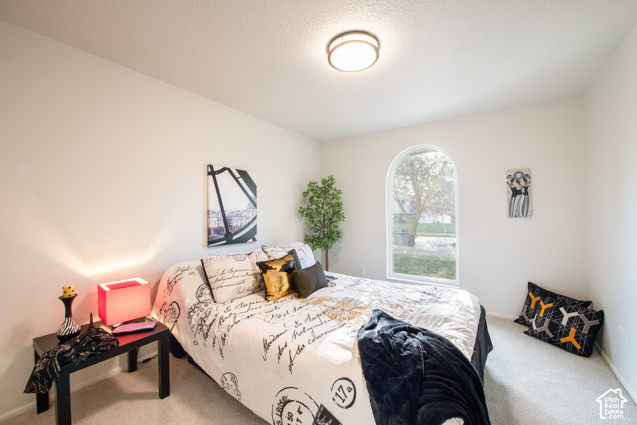 Furnished bedroom with an arched window, script-print bedding, and a red bedside lamp.