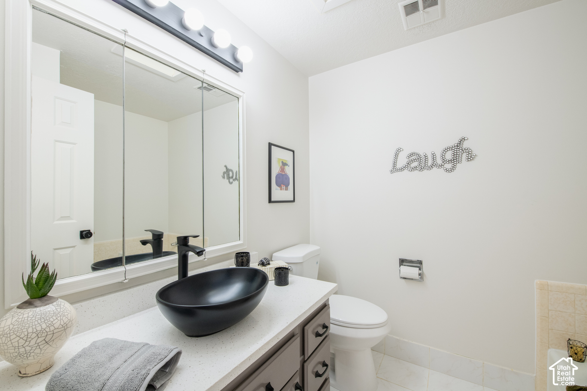Bathroom with a black vessel sink, gray vanity, large mirror, and toilet.