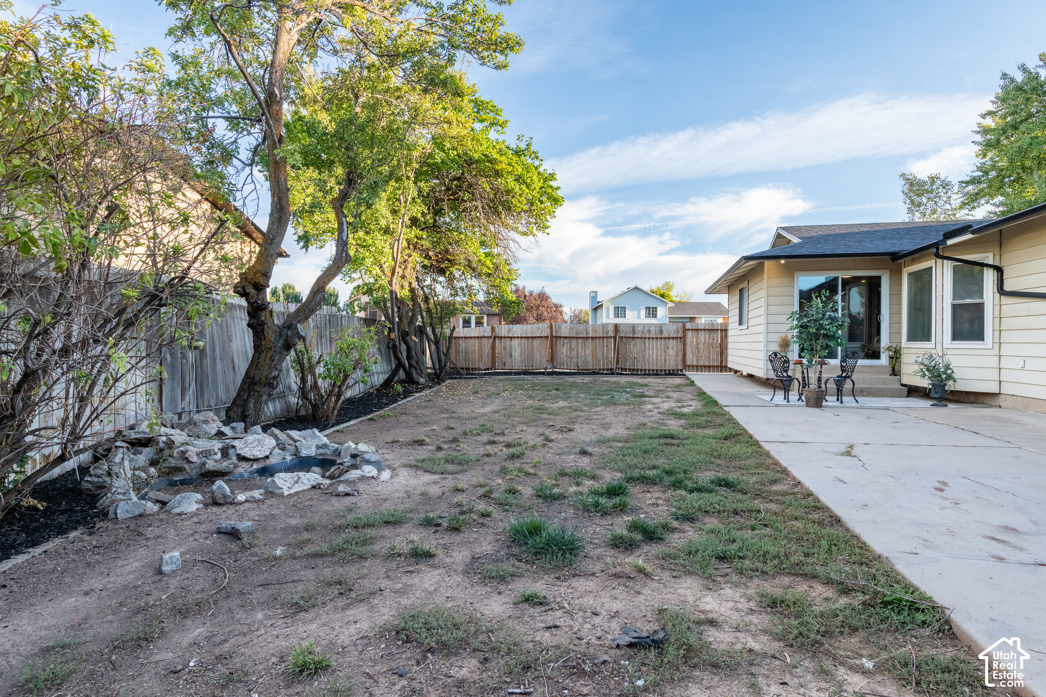Backyard with mature trees, a fenced yard, rock garden, and patio beside the house.