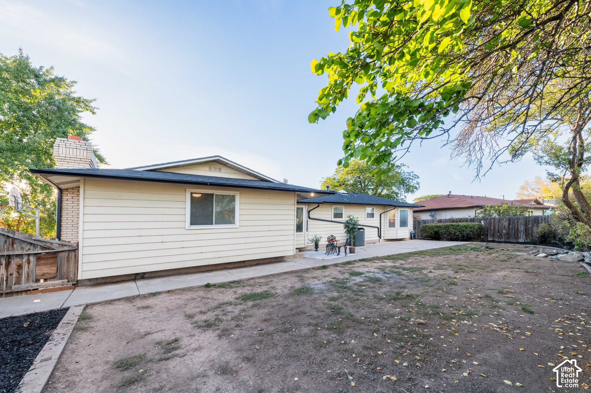 Rear of a single-story home with a fenced, mostly bare yard and small patio seating area.