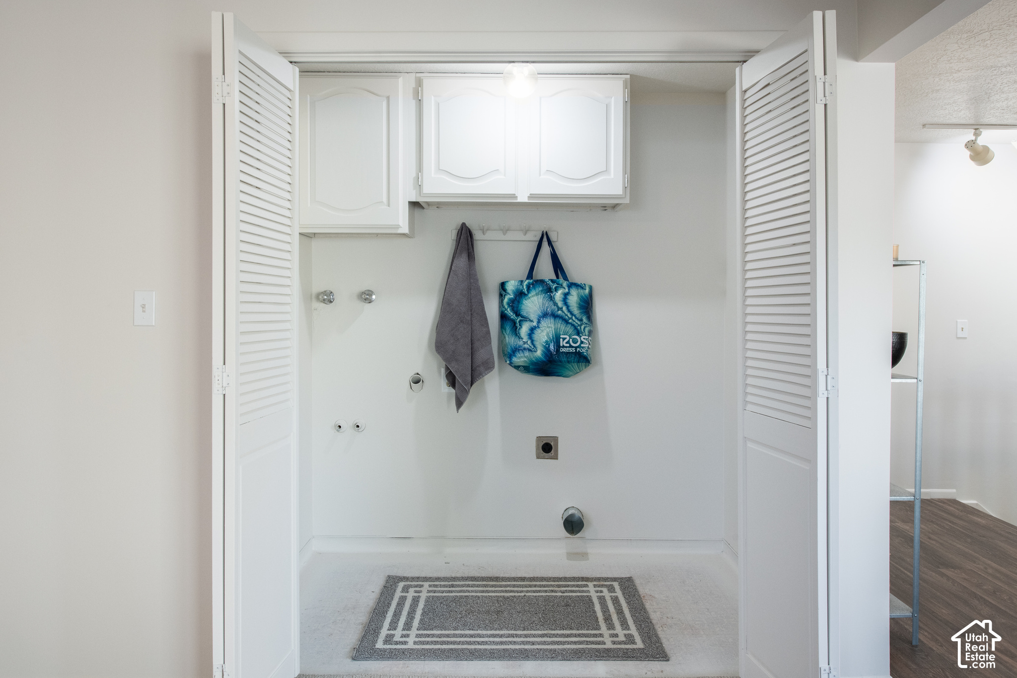 Laundry area with white cabinets, exposed appliance hookups, and open louvered doors.
