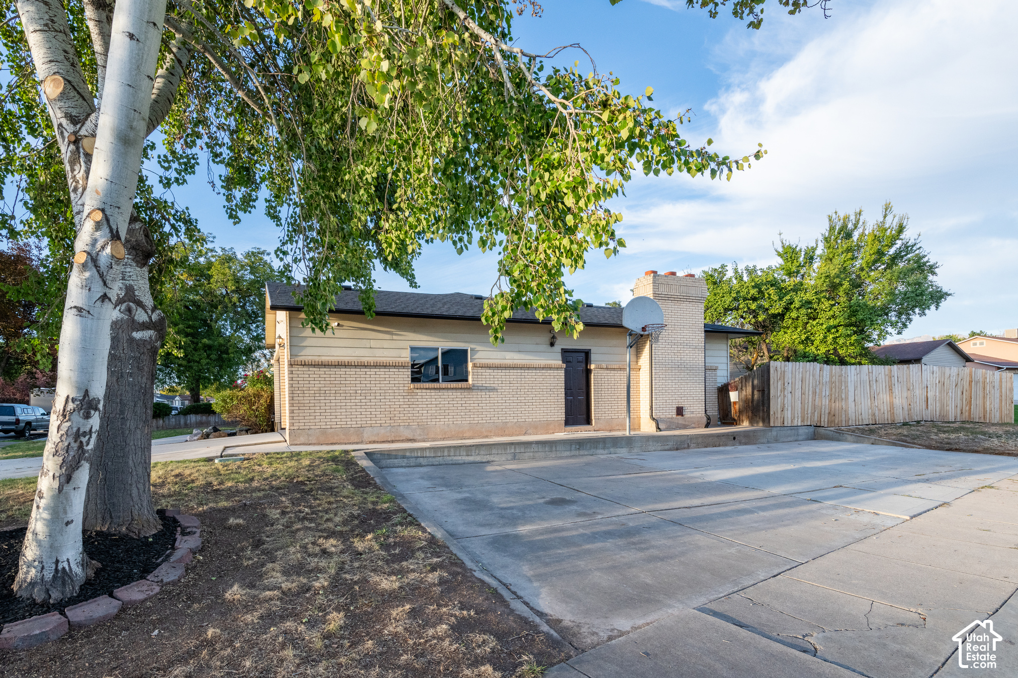 Single-story brick home with a wide driveway, basketball hoop, and mature trees.