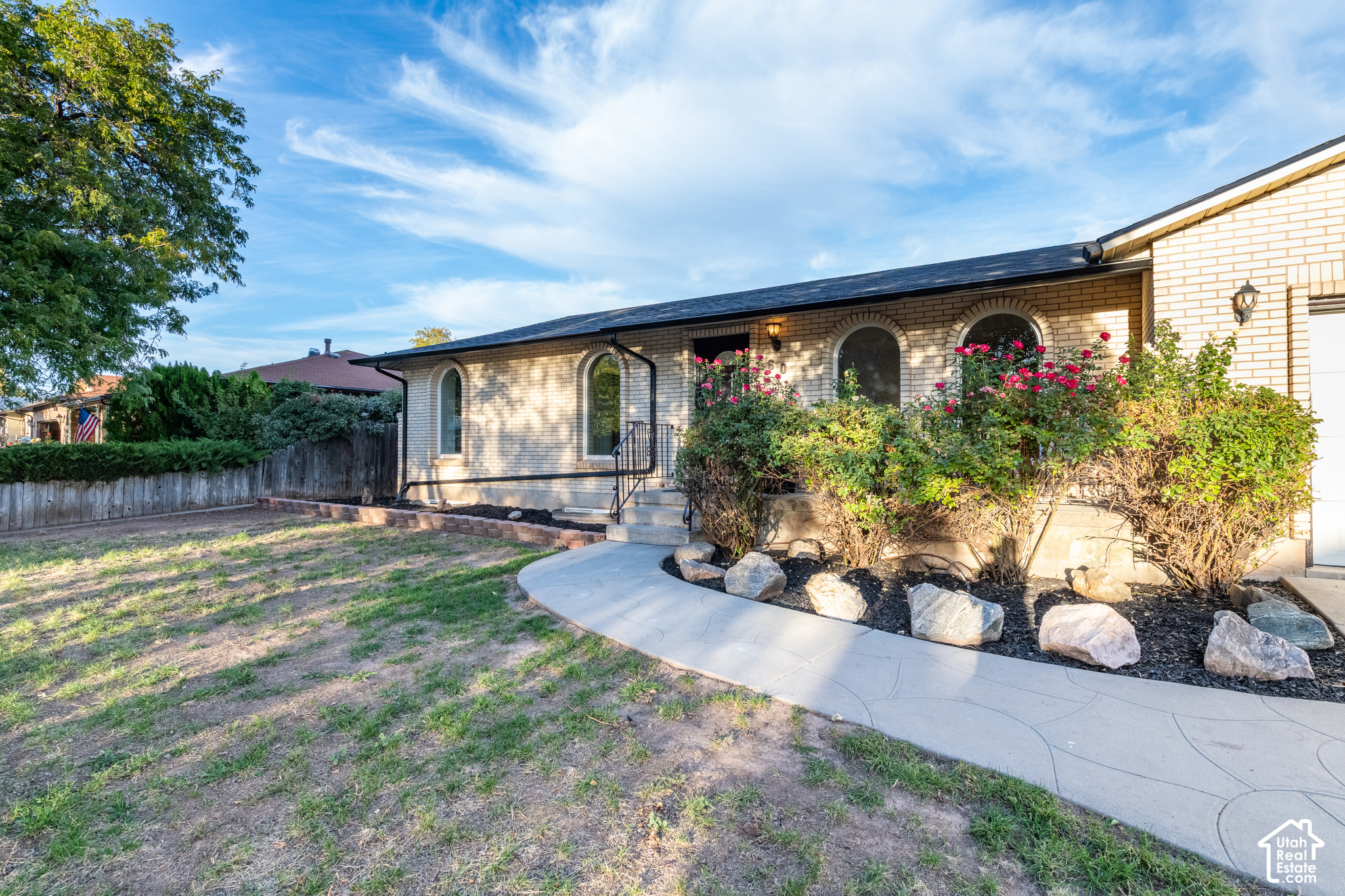 Light brick home with arched windows, rose bushes, and a curved concrete walkway.