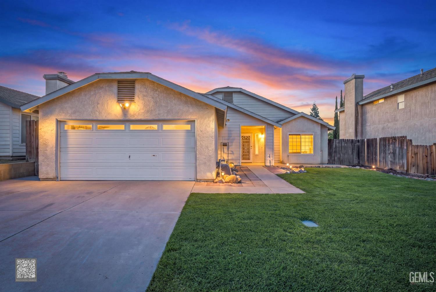 Single-story stucco house with a two-car garage and lit entry at dusk.