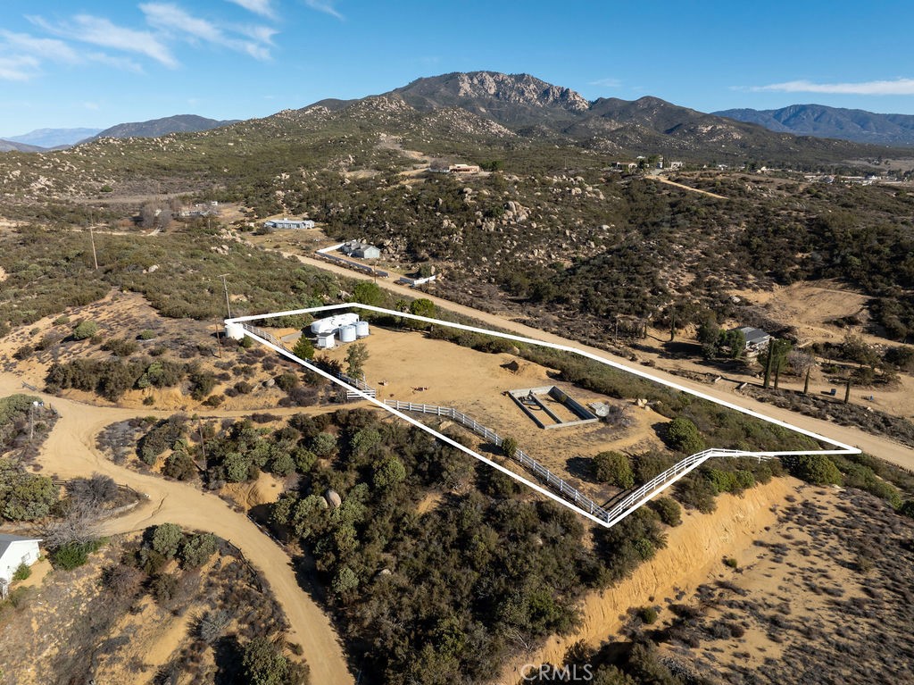 Aerial view of a fenced rural parcel with storage tanks and mountains beyond.
