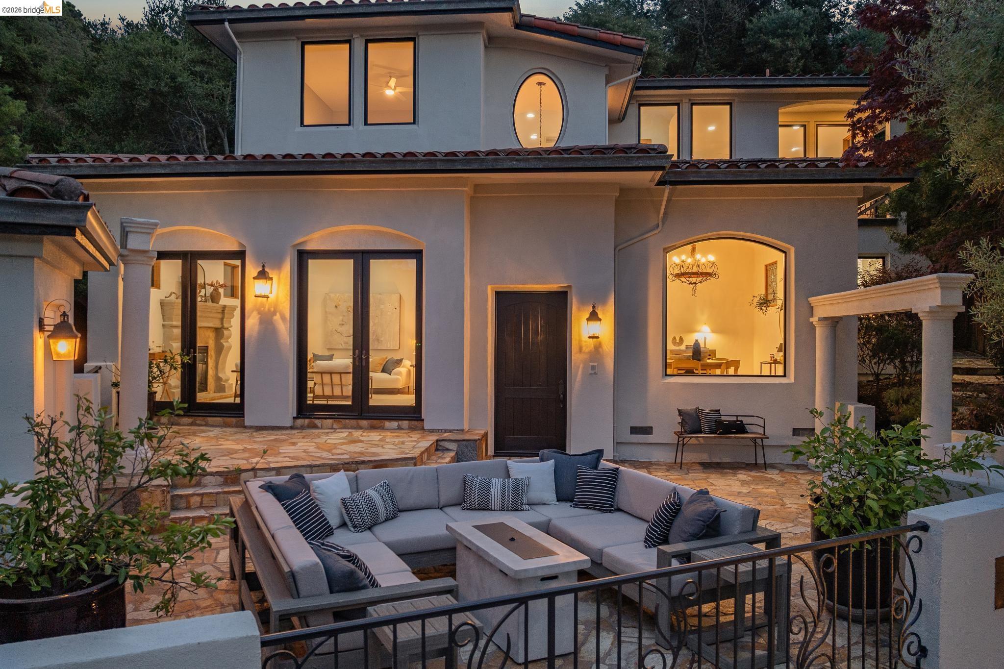 Two-story stucco home with arched windows and a furnished stone-paved courtyard at dusk.
