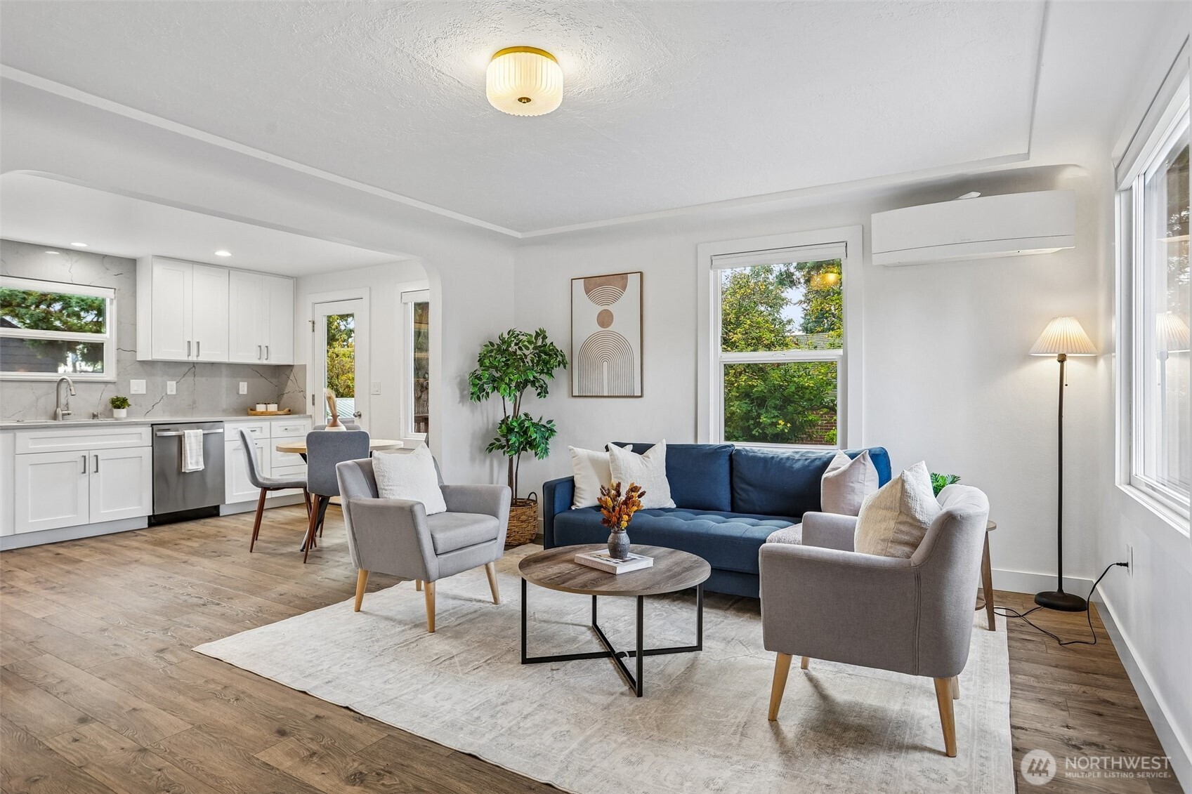 Open-plan living room and kitchen with a blue sofa, gray armchairs, and white cabinetry.