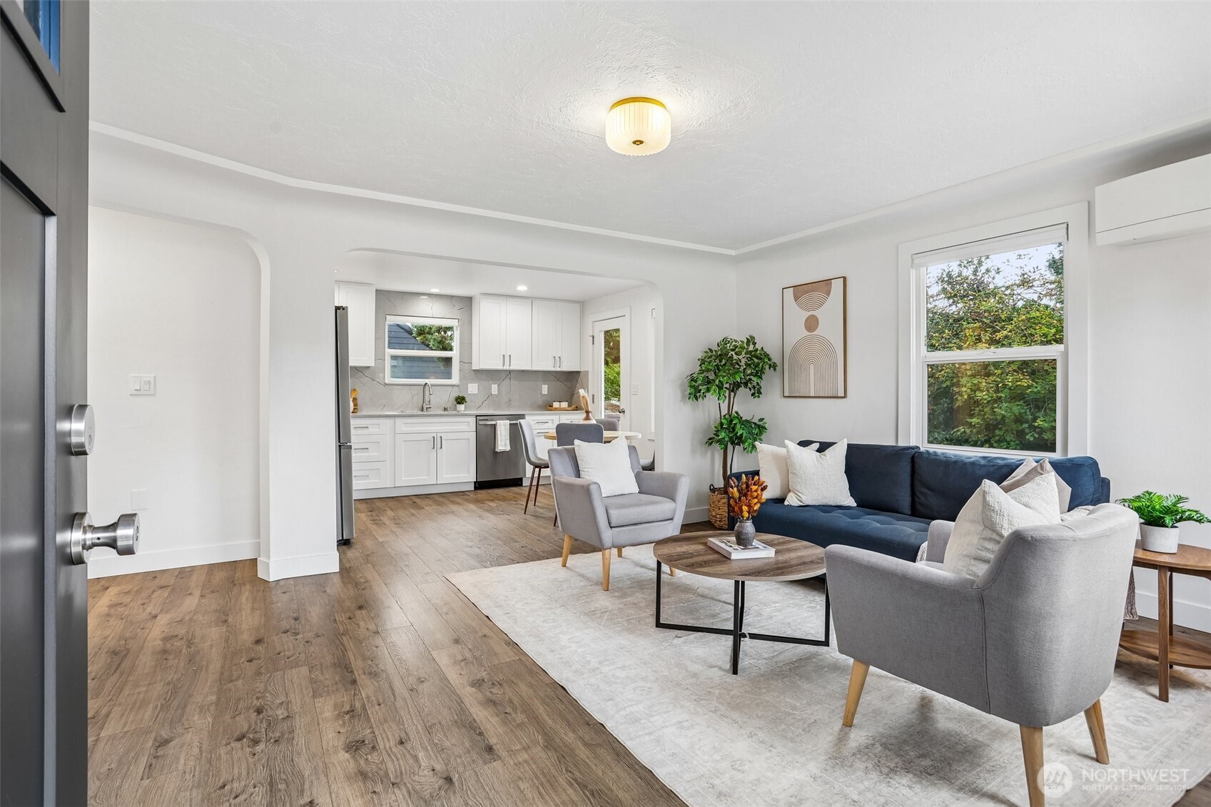 Staged open-plan living room and kitchen with navy sofa, gray armchairs, and white cabinetry.
