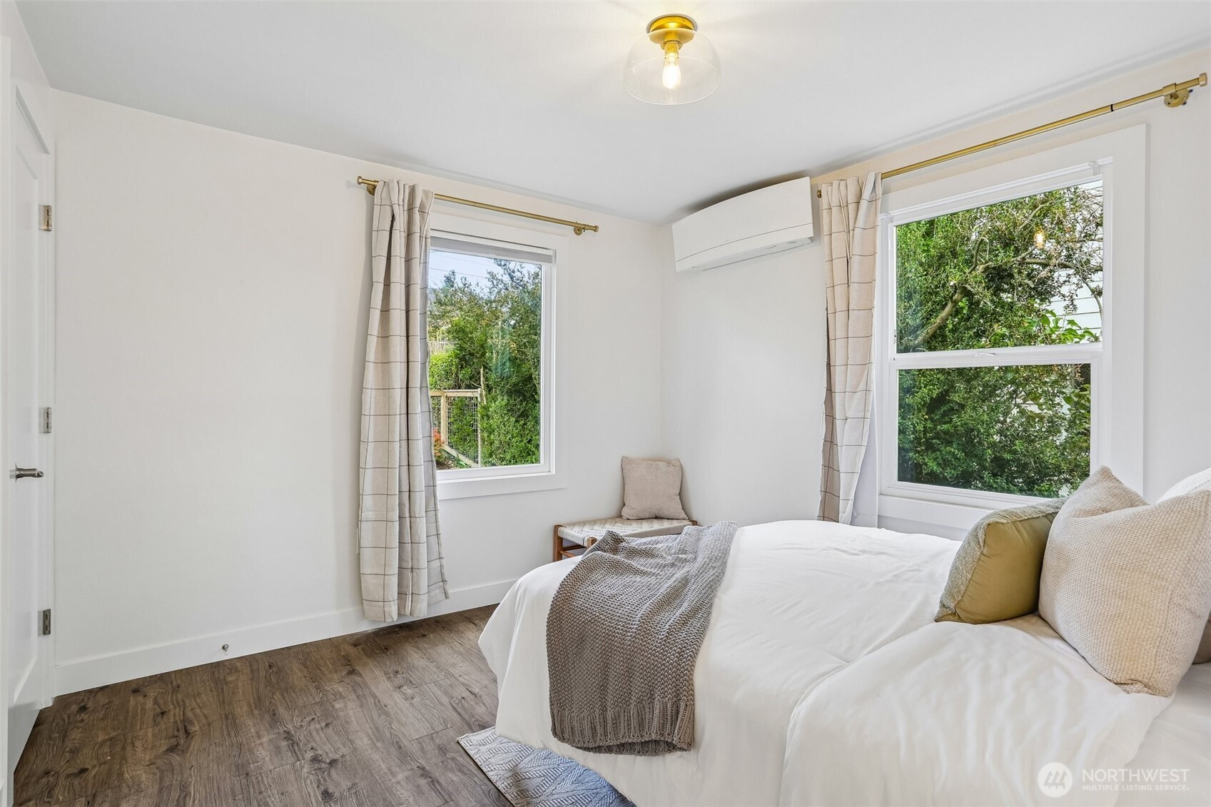 Furnished bedroom with a white bed, gray knit throw, two windows, and a wall-mounted mini-split.