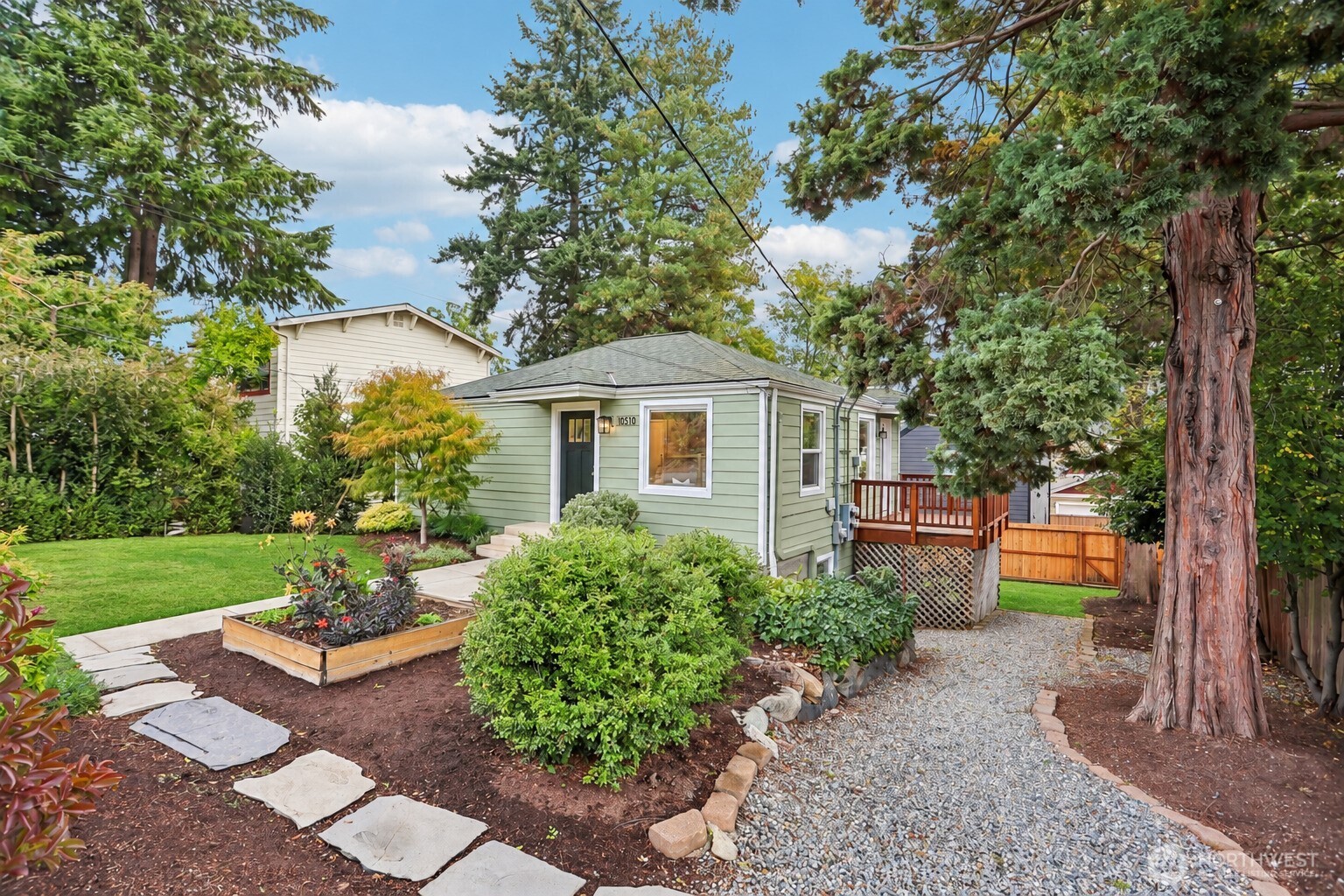 Pale green home with a small deck, landscaped garden, stepping-stone path, and mature trees.