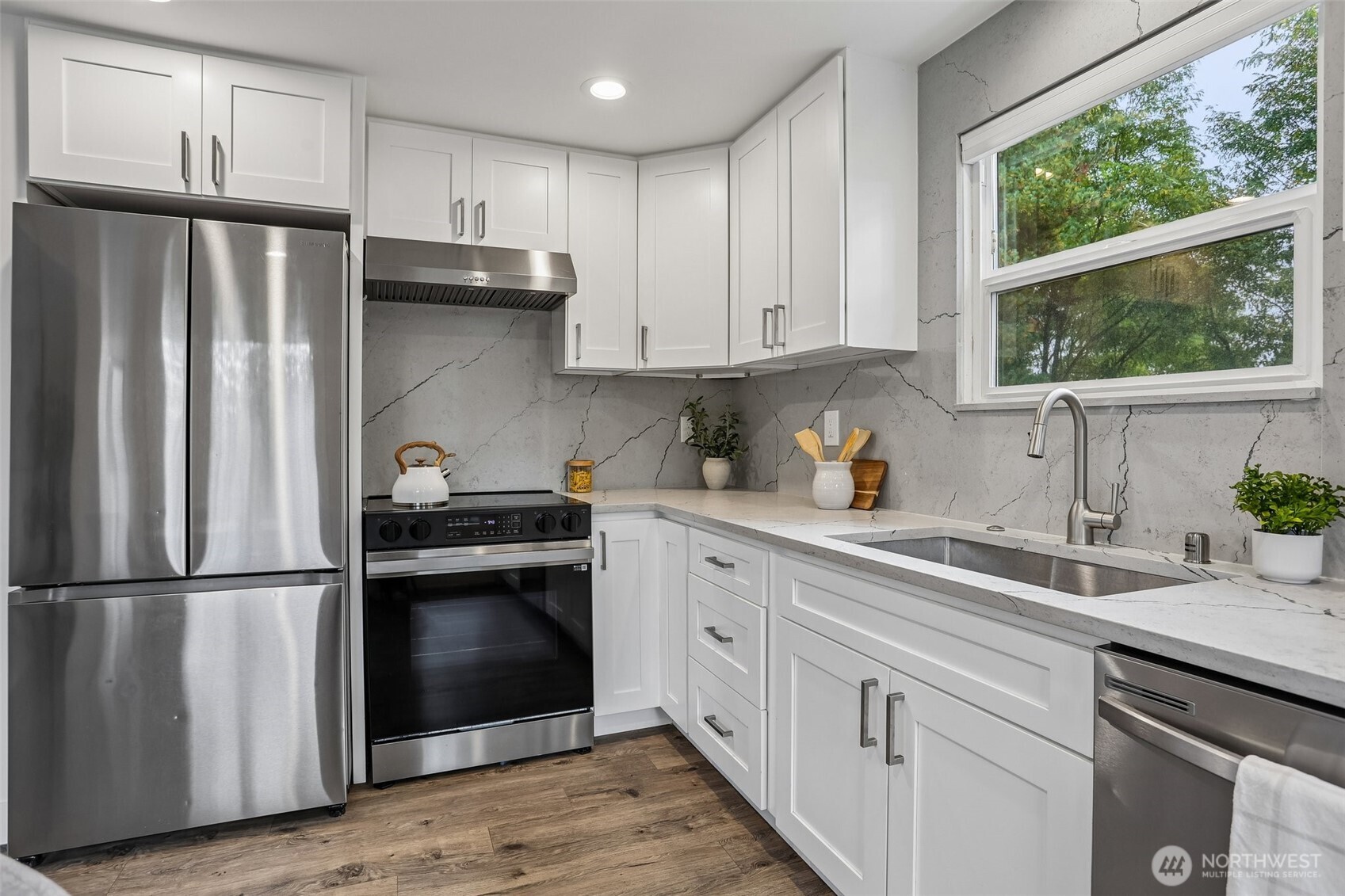 Kitchen with white cabinetry, veined stone counters, stainless steel appliances, and a large window.
