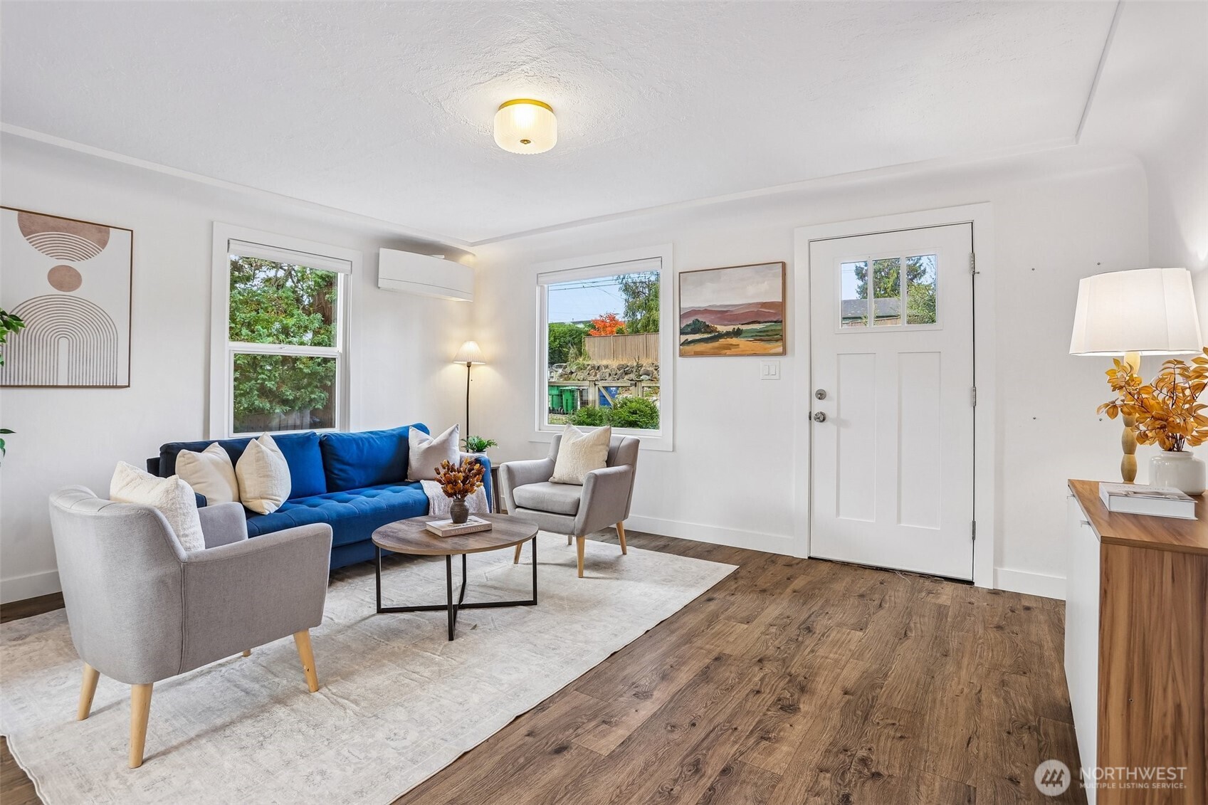 Staged living room with a blue sofa, gray armchairs, and wood-look flooring.