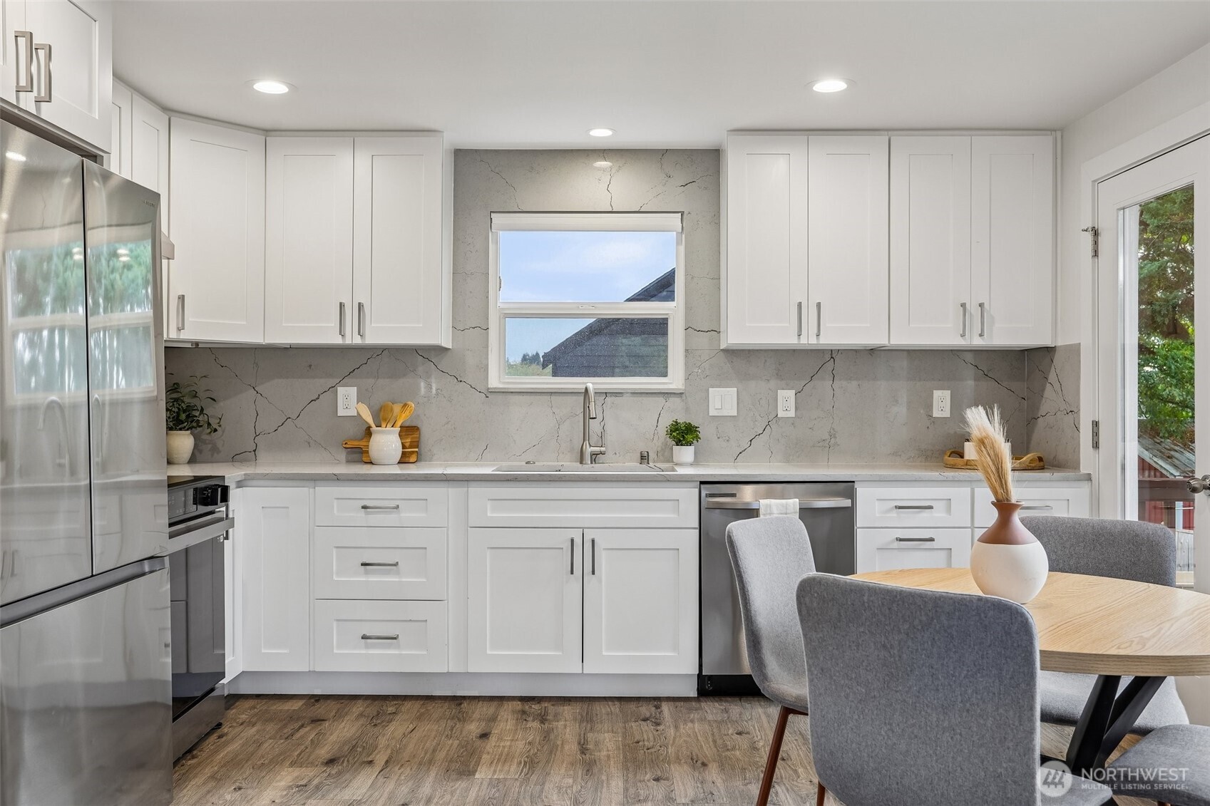 Bright kitchen with white cabinets, veined stone backsplash, stainless appliances, and a dining table.