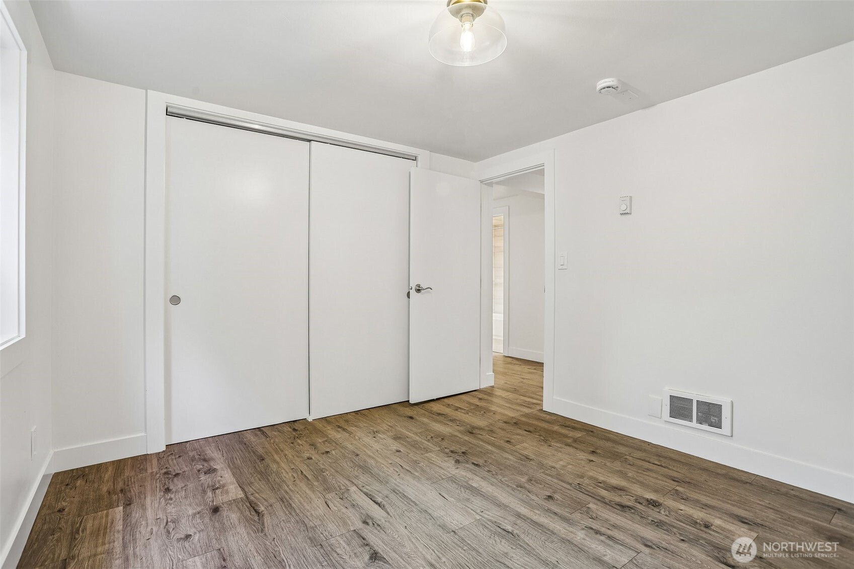 Empty bedroom with wood-look flooring and a large sliding-door closet.