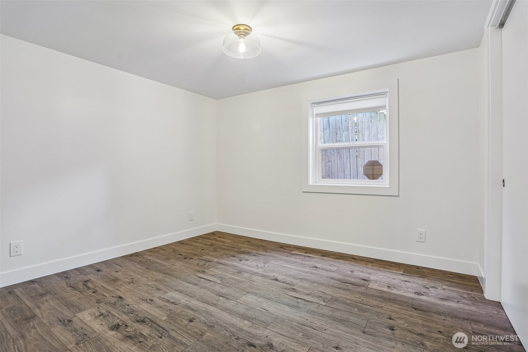 Empty bedroom with wood-look plank flooring and a window facing a wood fence.