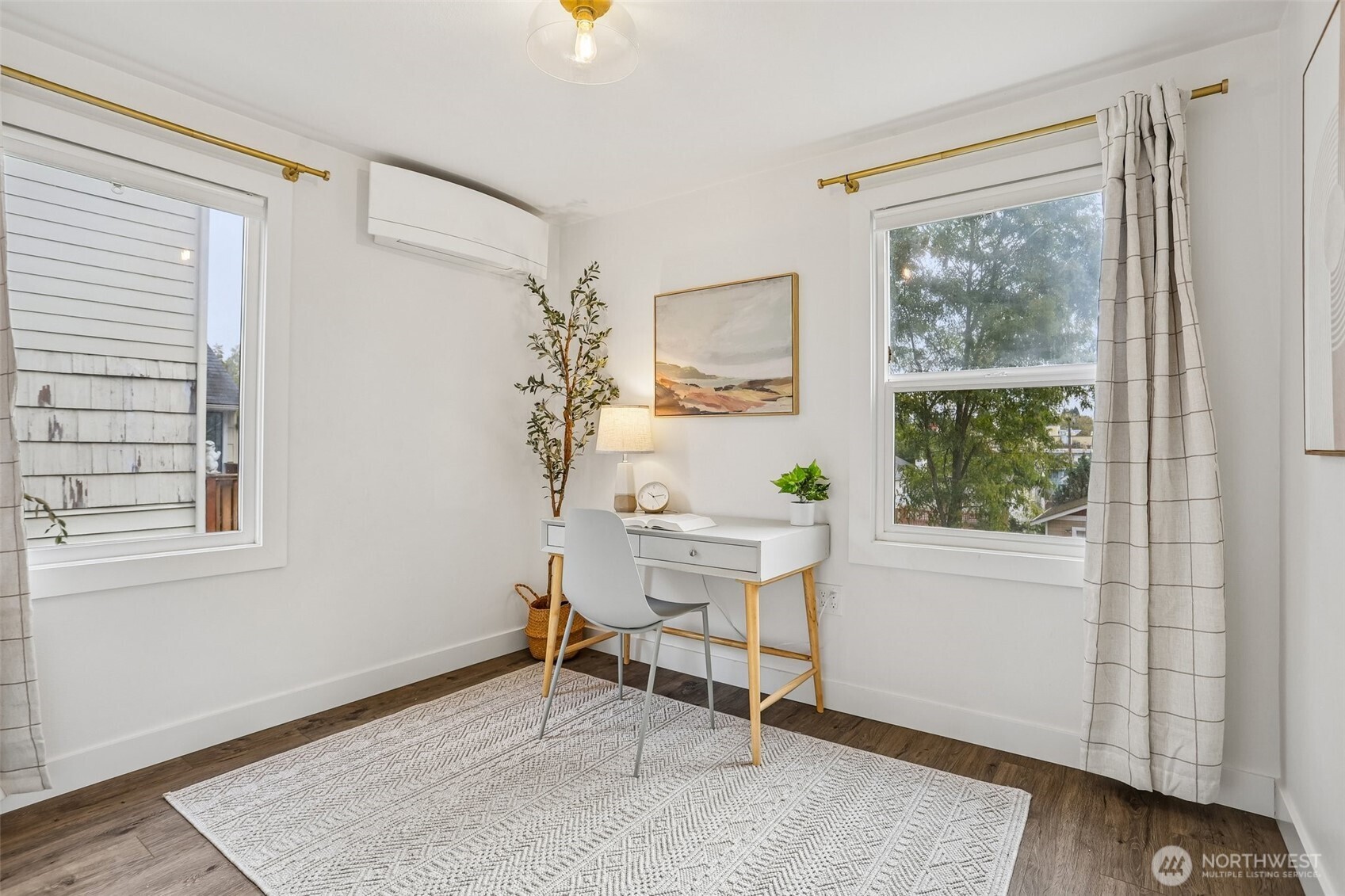 Staged home office with a white desk between two windows and a patterned rug.
