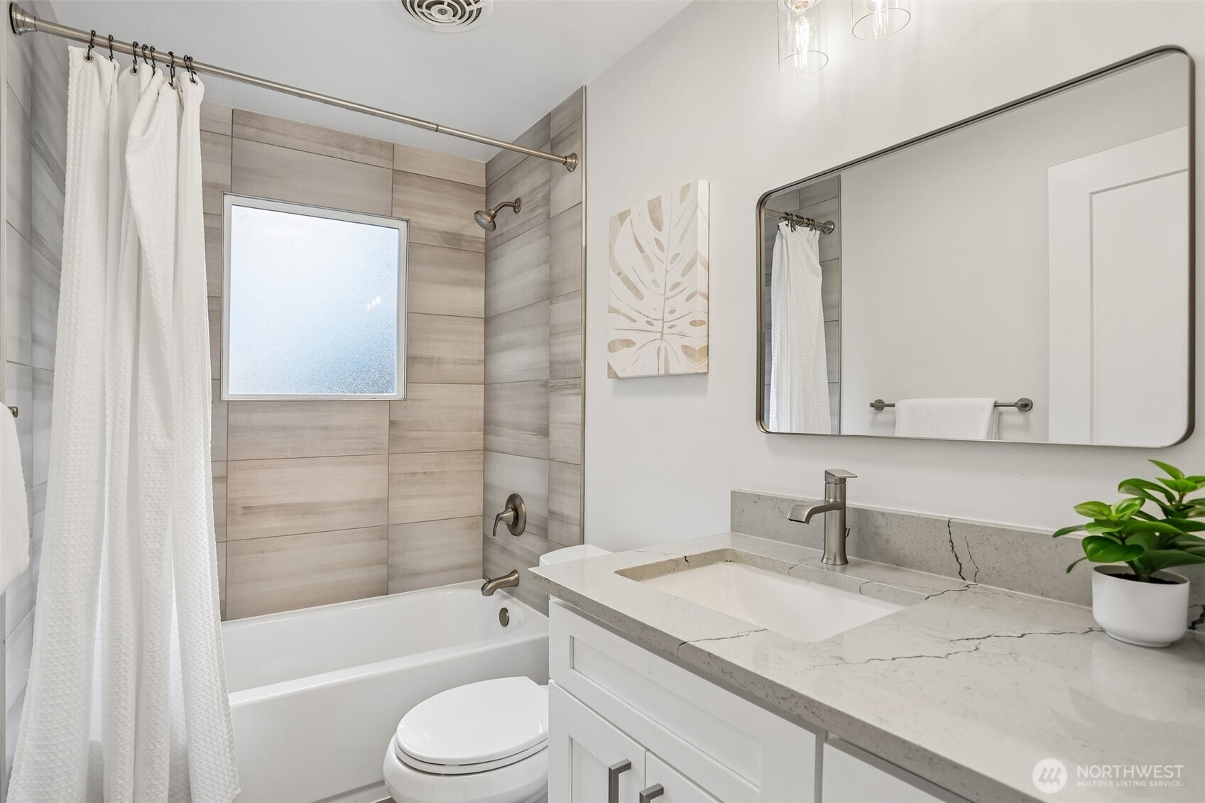 Bathroom with tiled tub surround, white vanity, veined stone countertop, and wide mirror.