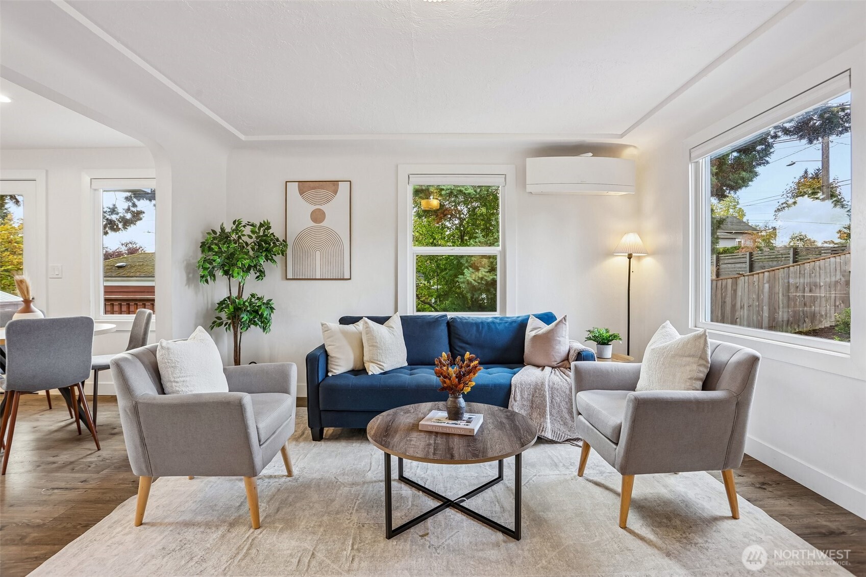 Staged living room with a blue sofa, gray armchairs, and large windows.