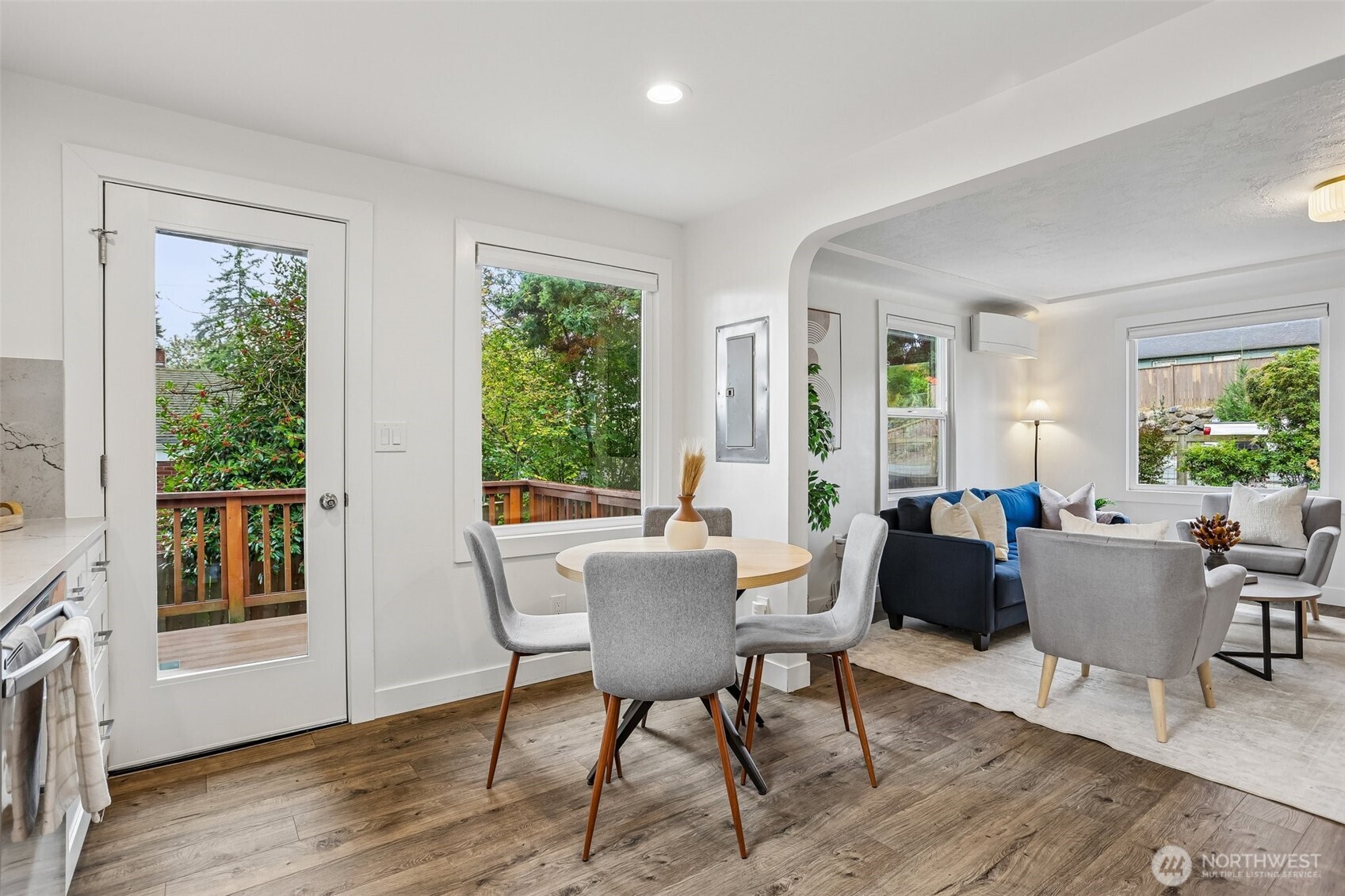 Open-plan dining and living room with a round table, blue sofa, and glass door to a deck.