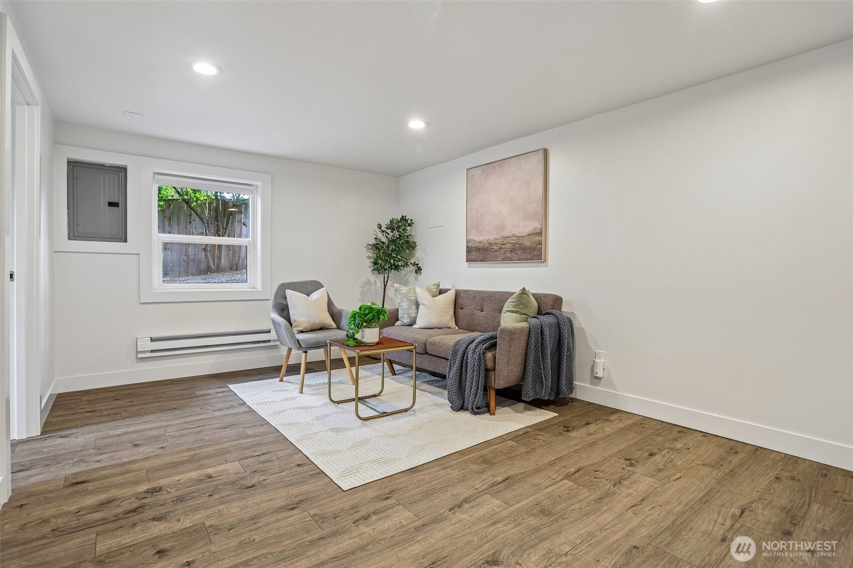 Staged living room with gray sofa, armchair, wood-look floors, and a window.