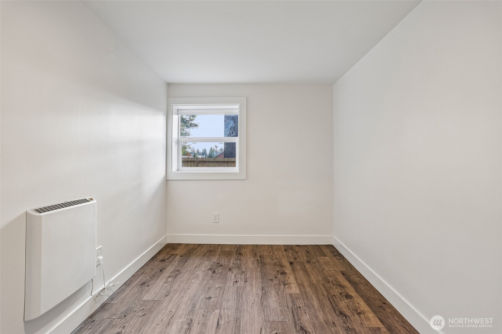 Vacant room with wood-look flooring, a small window, and a wall-mounted heater.