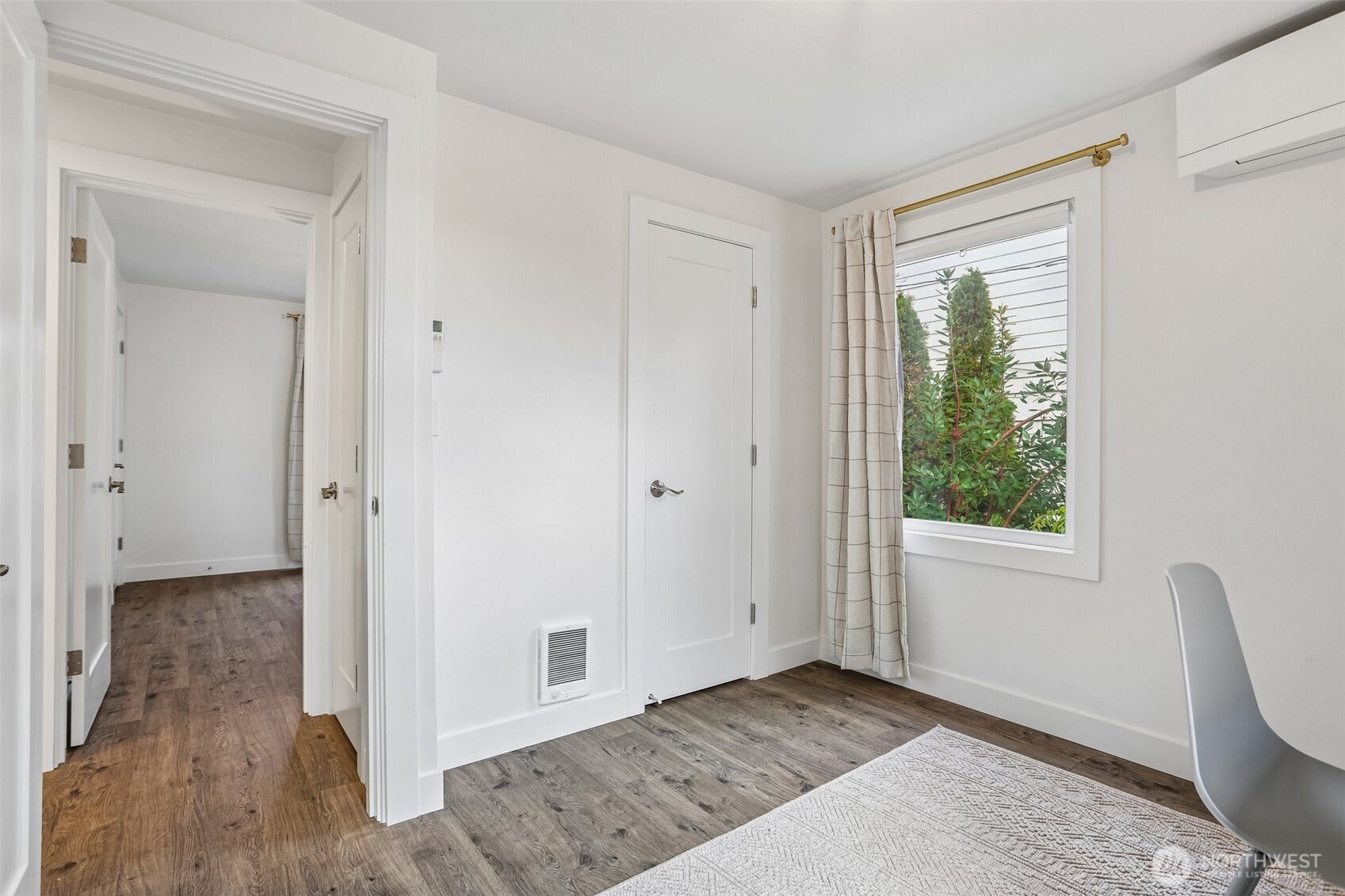 Bright room with wood-look flooring, a curtained window, white chair, and rug.