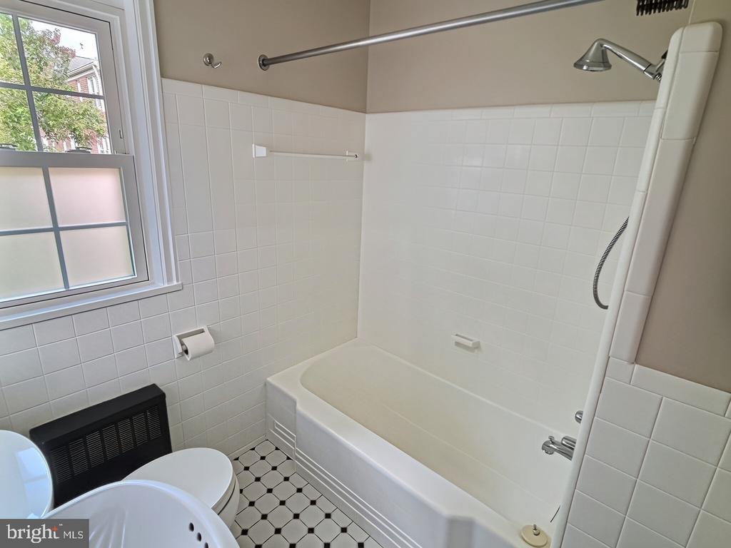 Bathroom with a tiled tub and shower, window, and black-and-white hexagonal floor.