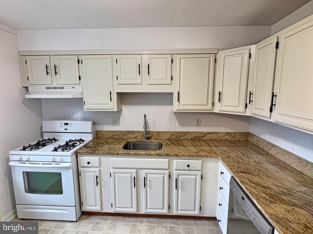 Kitchen with white cabinets, tan granite counters, a gas range, and a stainless-steel dishwasher.