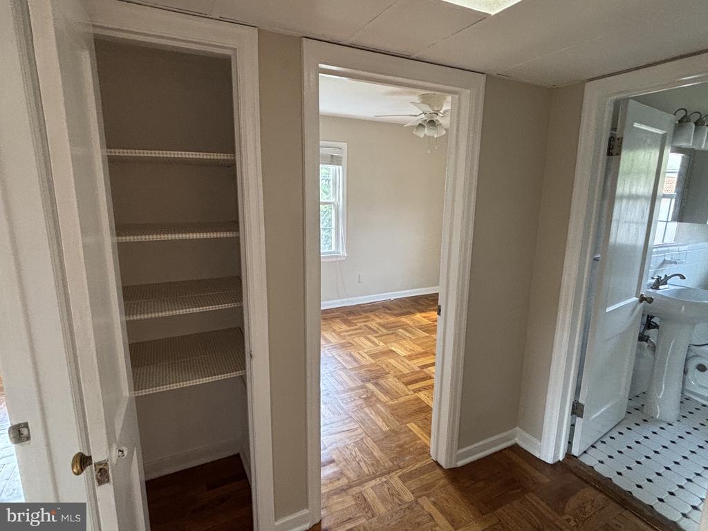 Hallway with parquet flooring, an open linen closet, and doorways to a bedroom and bathroom.