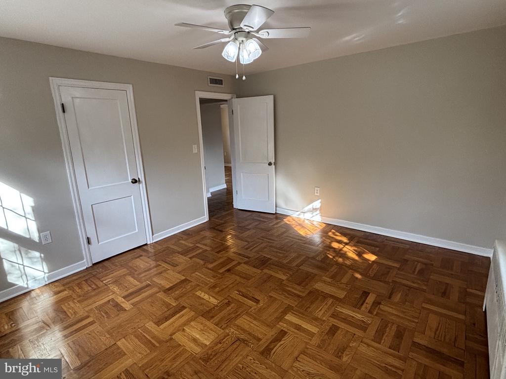 Empty room with patterned parquet flooring, white doors, and a ceiling fan.