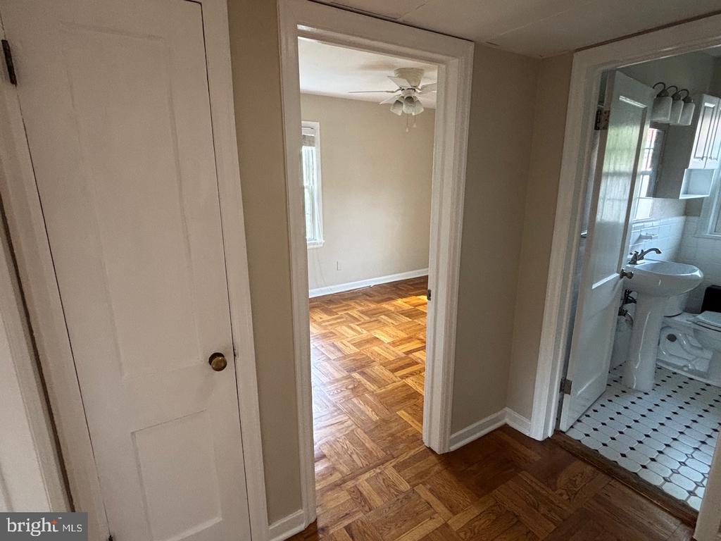Hallway with parquet floors opening to an empty room and a bathroom with black-and-white tile.