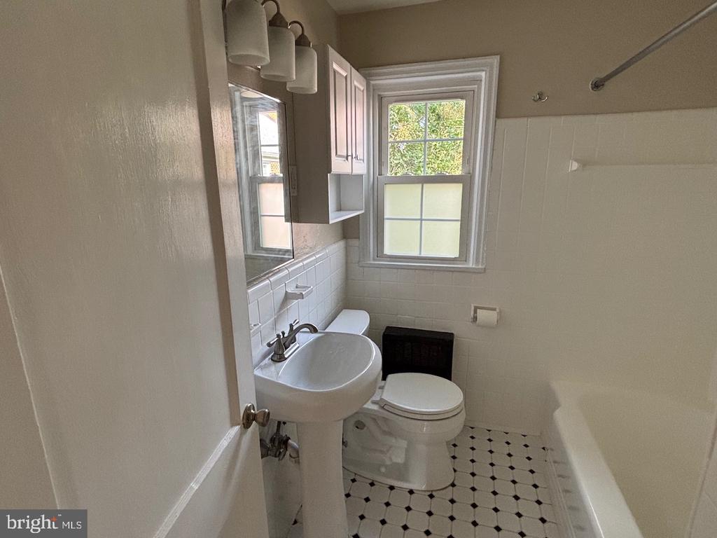 Bathroom with a pedestal sink, bathtub, and black-and-white patterned floor beneath a window.