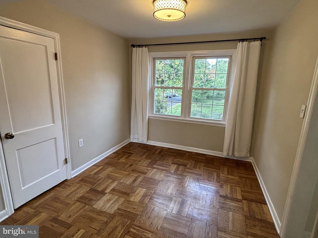 Empty room with parquet flooring, a curtained window, and a ceiling light.