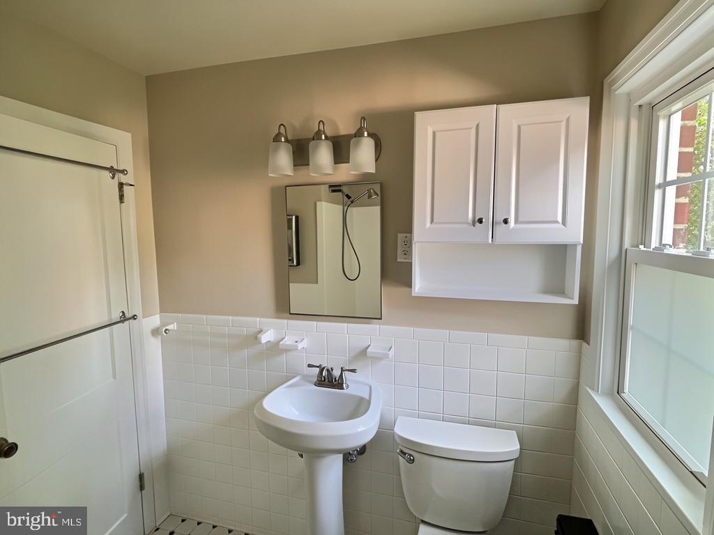 Bathroom with pedestal sink, toilet, tiled walls, and a large window.