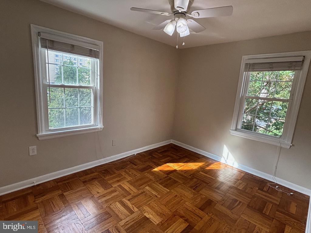 Vacant bedroom with parquet floors, two windows, and a ceiling fan.