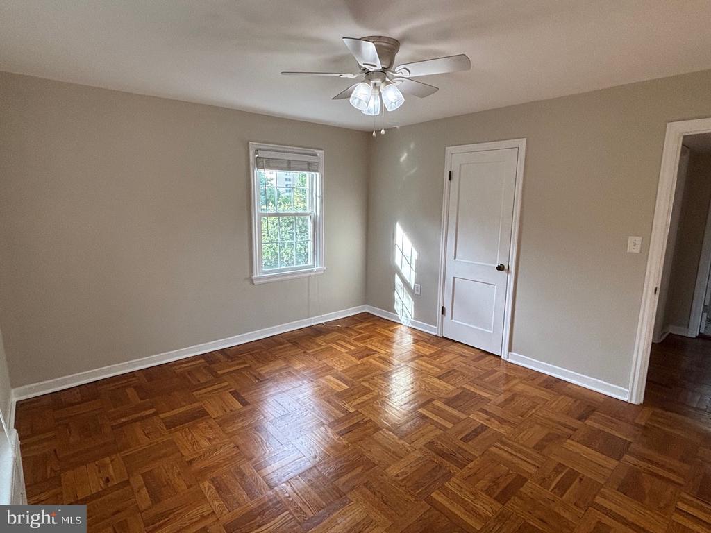 Empty bedroom with parquet wood flooring, a ceiling fan, and a sunlit window.