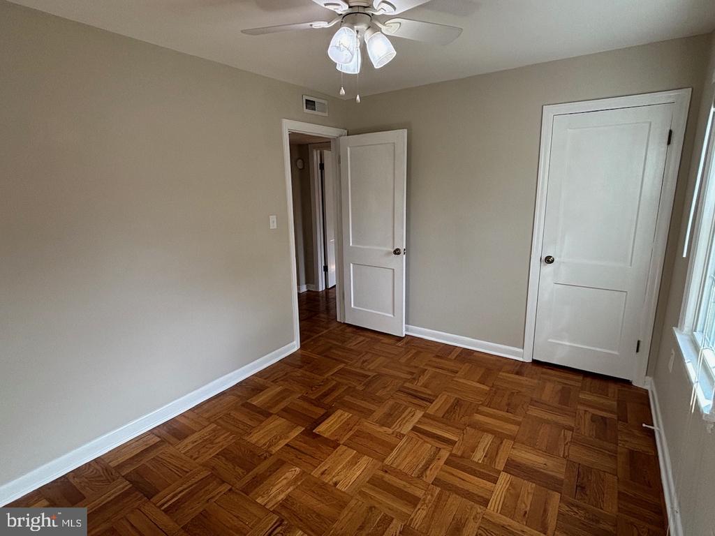 Empty bedroom with parquet flooring, a ceiling fan, and two white doors.