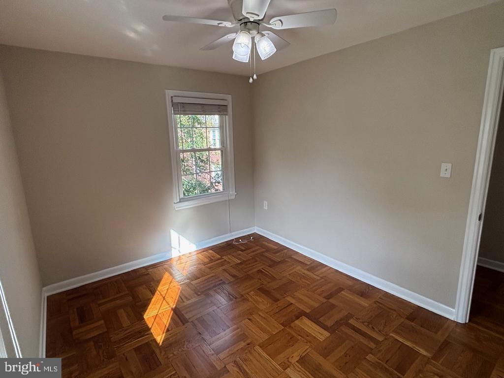 Empty room with parquet hardwood flooring, a ceiling fan, and sunlight through the window.
