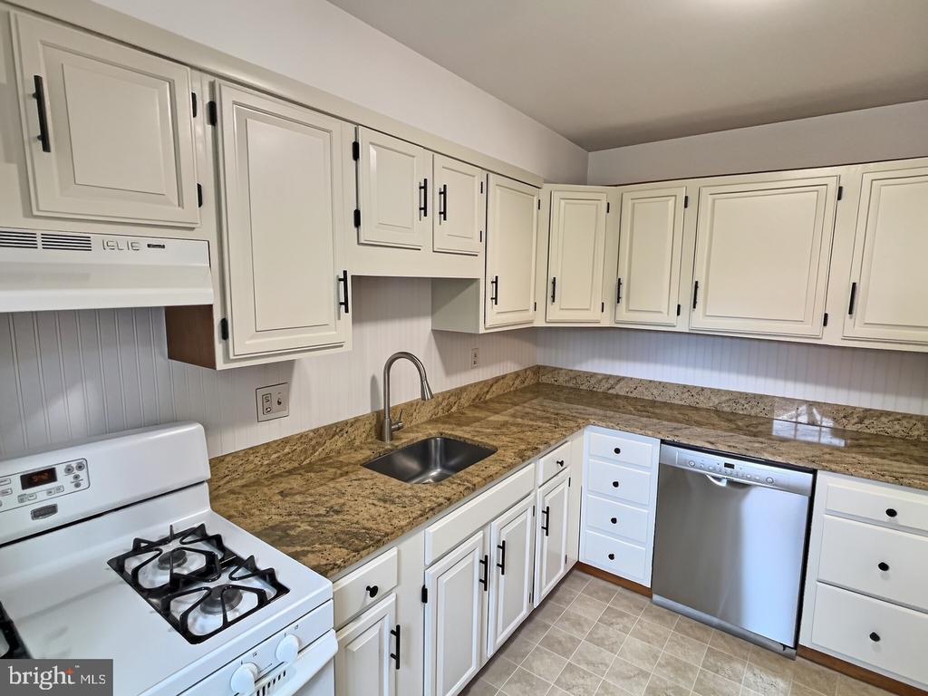 Kitchen with white cabinets, brown granite counters, a gas range, and stainless-steel dishwasher.